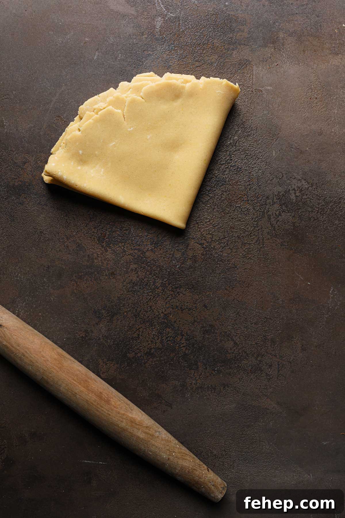 Italian Pasta Frolla Shortcrust Pastry: Multipurpose Dough Guide 15 Rolled dough folded over itself in a triangle shape next to a rolling pin.