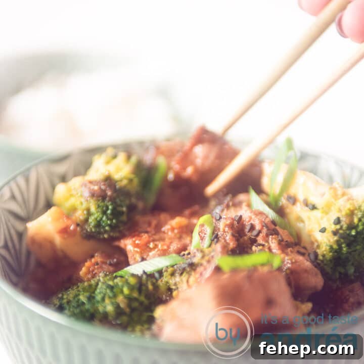 A square photo where two chopsticks take a cube of steak from a green bowl filled with broccoli, steak and sauce.