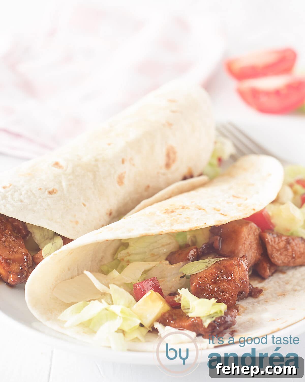 Soy Chicken Wrap Recipe: Flavorful Plant-Based Lunch Ideas 4 Two wraps, one of which is half open. There you can see chicken, iceberg lettuce and tomato. A white background. A canvas and some tomato wedges can be seen in the background.