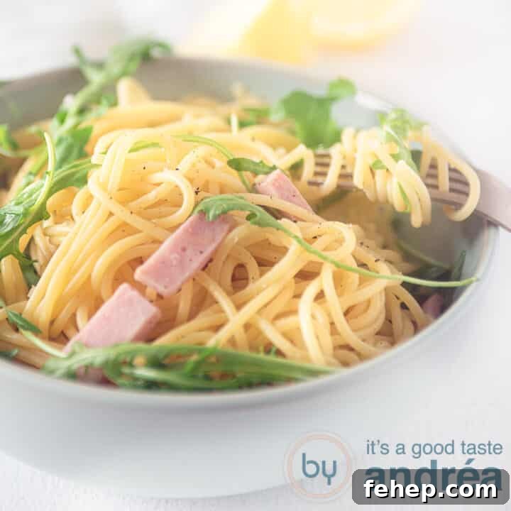 A square photo net a gray bowl filled with ham, arugula and spaghetti on a white background