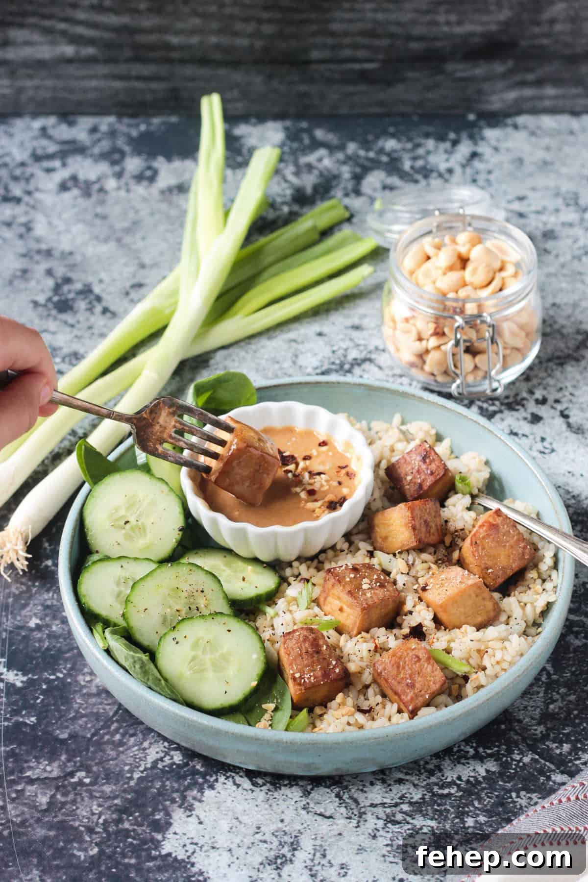 Flavorful Marinated Baked Tofu Recipe for Crispy, Savory Tofu 8 Bite-sized baked tofu square on a fork being dipped into peanut sauce.