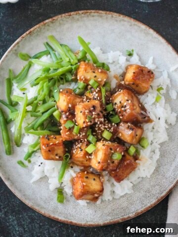 Baked sesame ginger tofu plated over rice with a side of green beans.