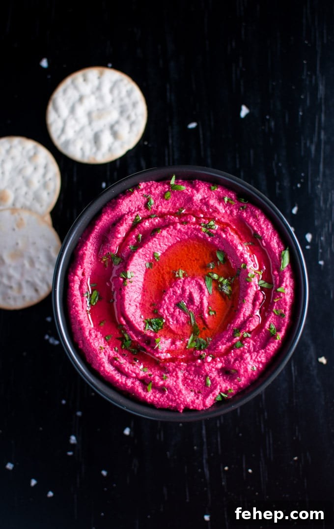 black bowl with roasted beet hummus topped with parsley and olive oil beside crackers