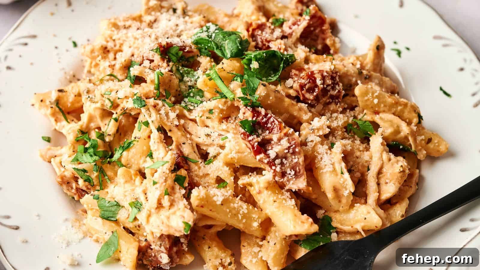 11 Marry Me Recipes That Impress Without Fuss 7 A plate of creamy penne pasta garnished with chopped parsley and grated cheese, featuring pieces of sun-dried tomatoes. A black fork is resting on the plate.