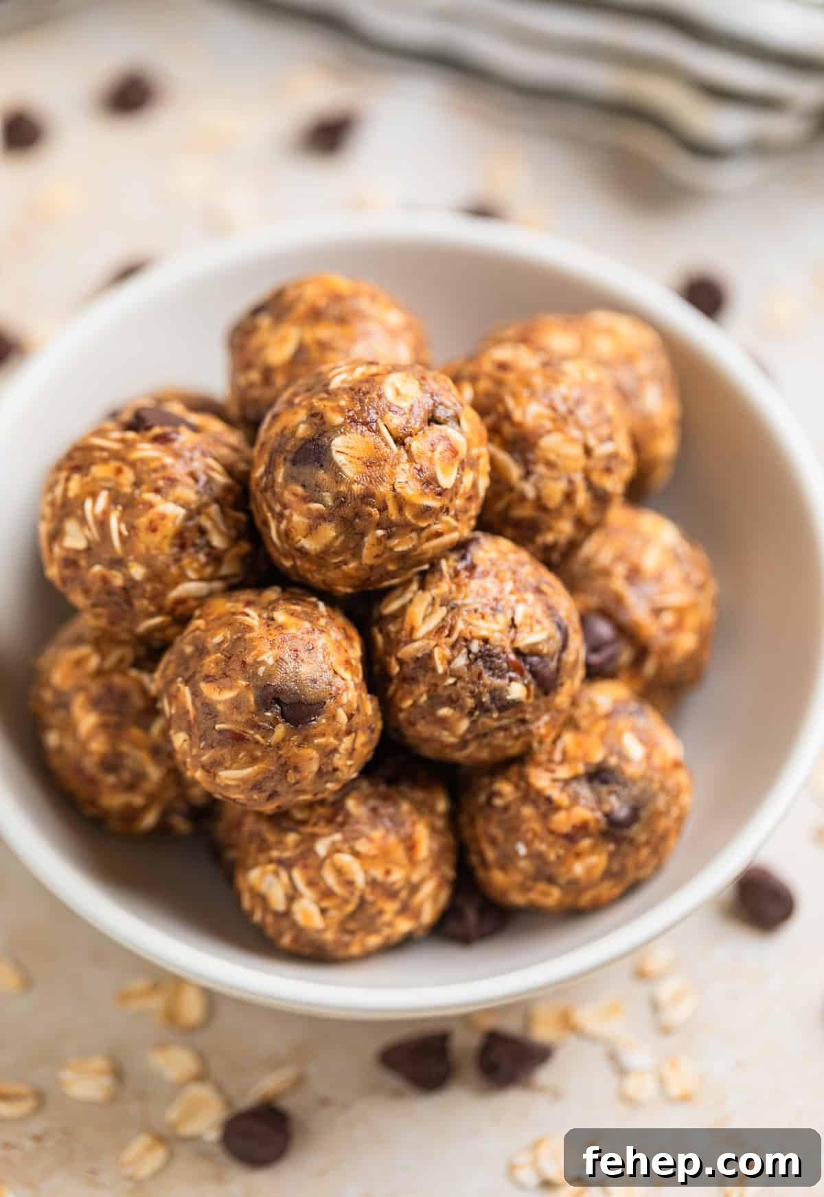 White dish with no bake oatmeal peanut butter balls with rolled oats and chocolate chips surrounding.