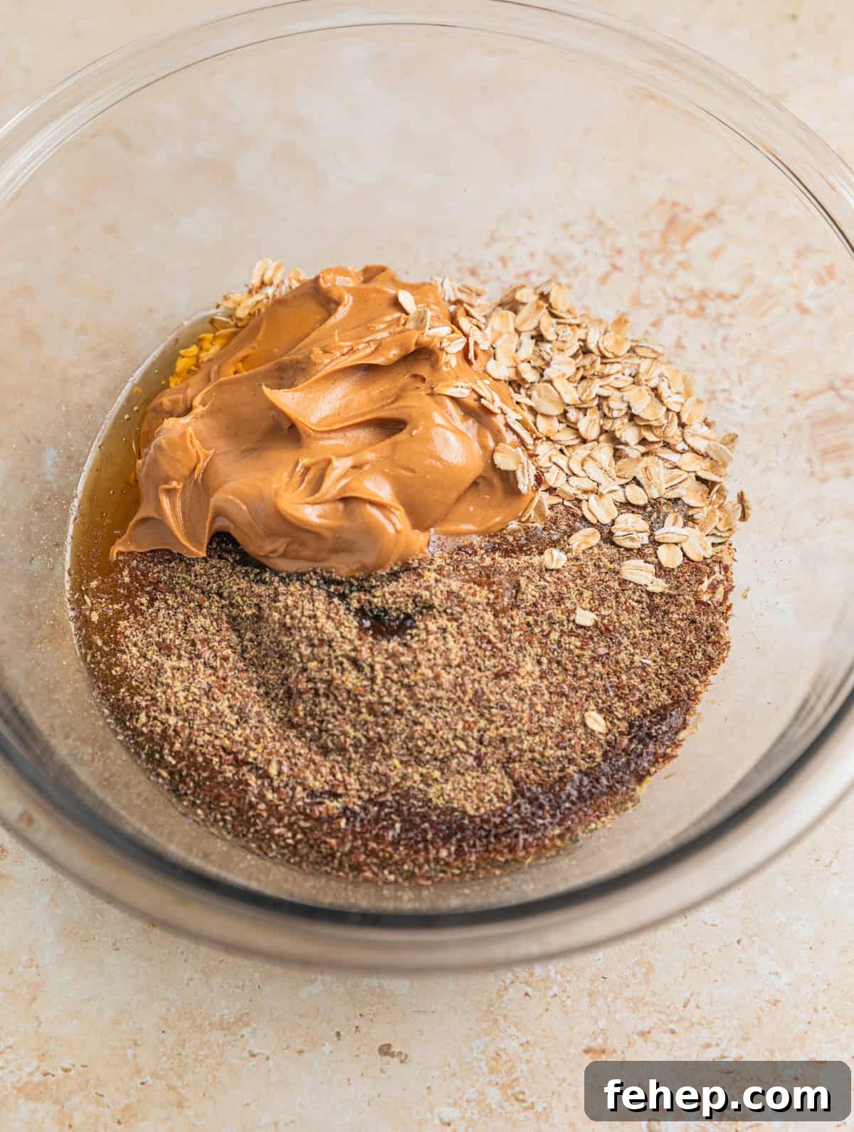 Peanut butter, oats, flax, maple and honey in glass mixing bowl.