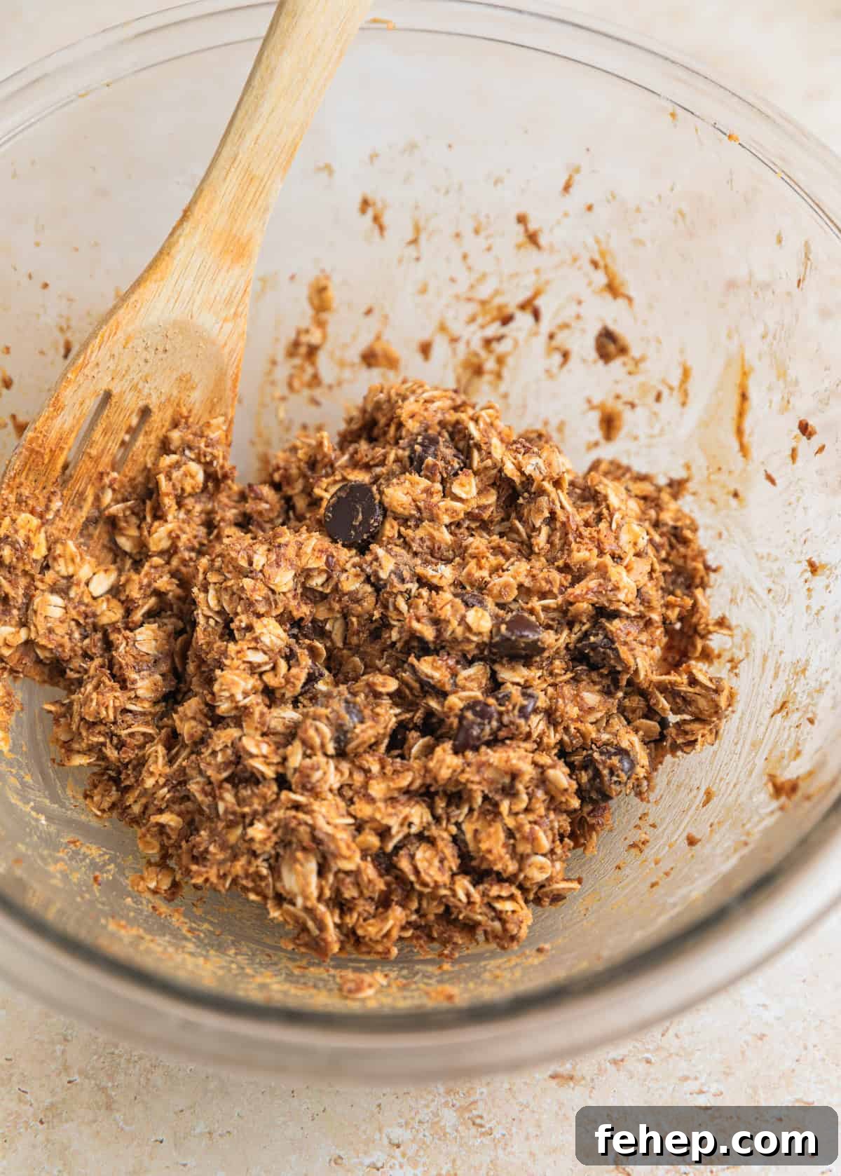 Chocolate chips stirred into oat mixture in glass bowl with wooden spoon.