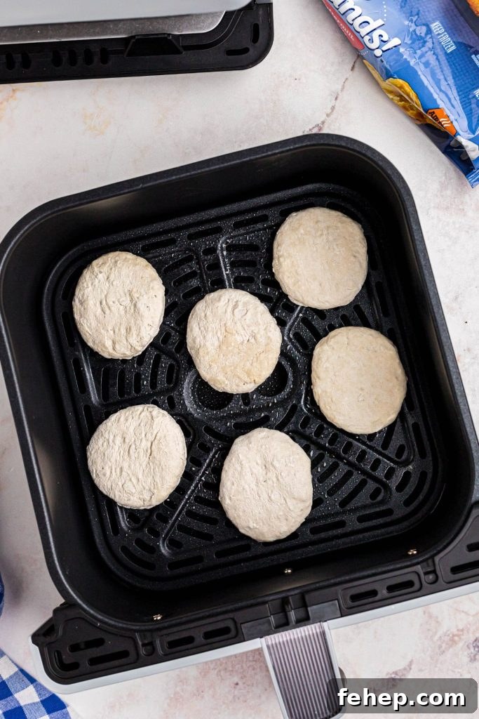 Crispy Air Fryer Frozen Biscuits in Minutes 4 Frozen biscuits in the air fryer basket on a white marble table.