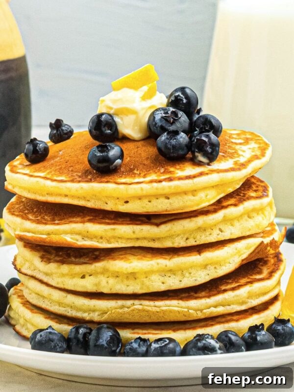Golden fluffy pancakes stacked on a white plate, topped with blueberries and butter.