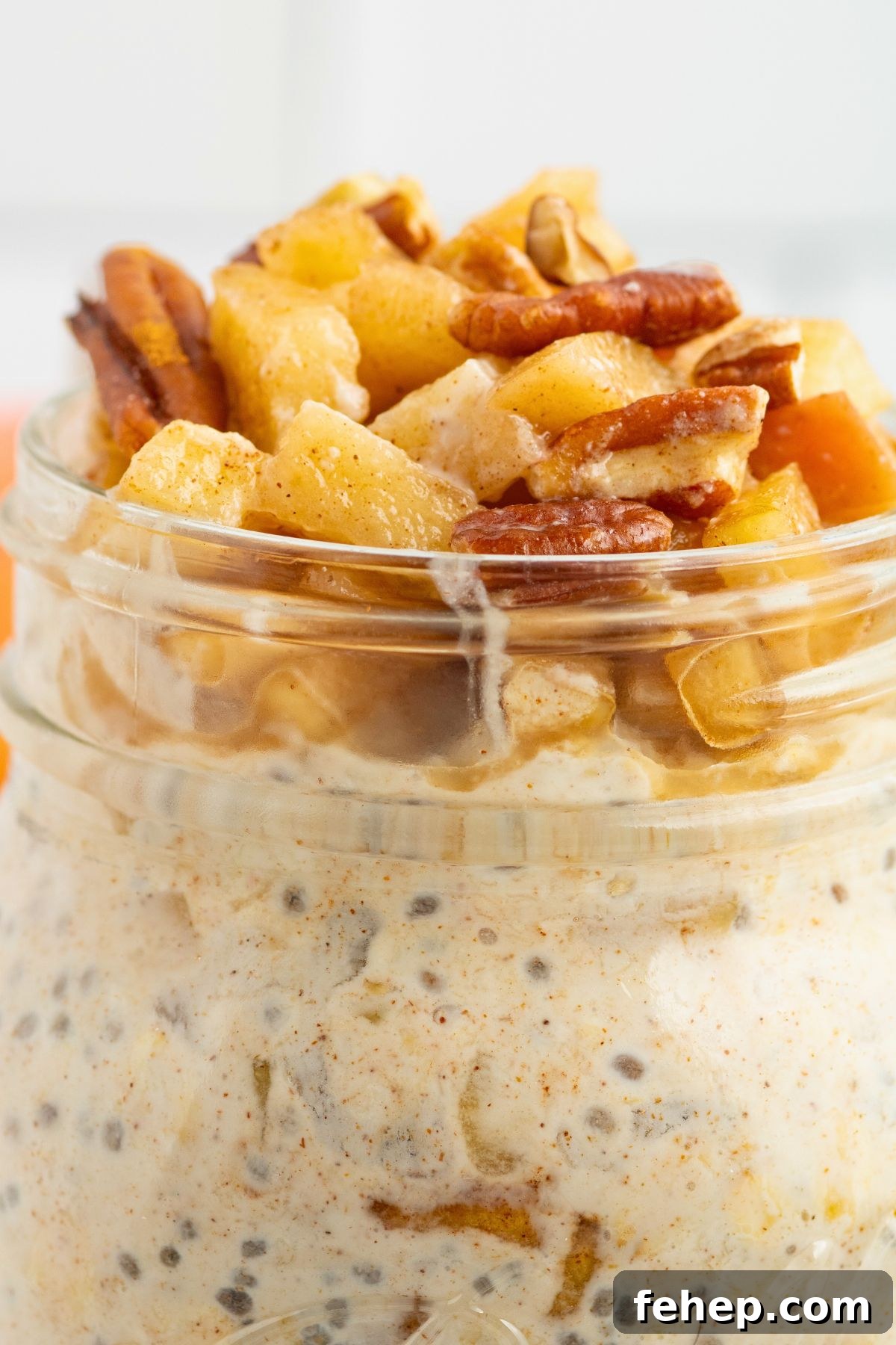 Close up photo of apple pie overnight oats in a mason jar, topped with crushed nuts and apples. 
