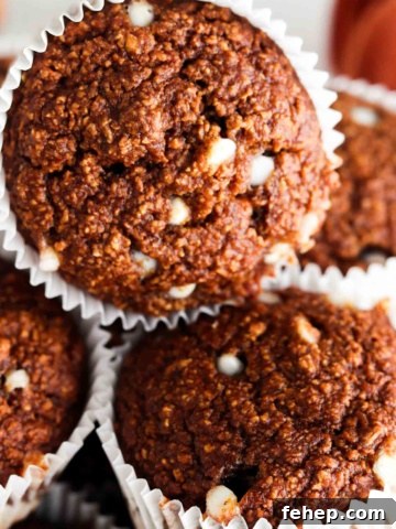 Close up photo of oat flour muffins stacked on top of each other with white chocolate chips on top.