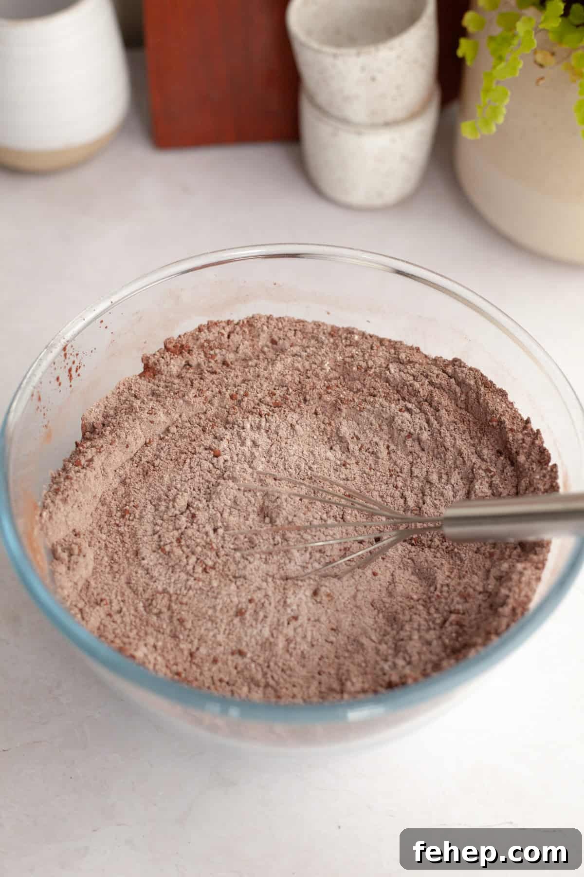 Flour and cocoa powder in a glass bowl with a whisk.