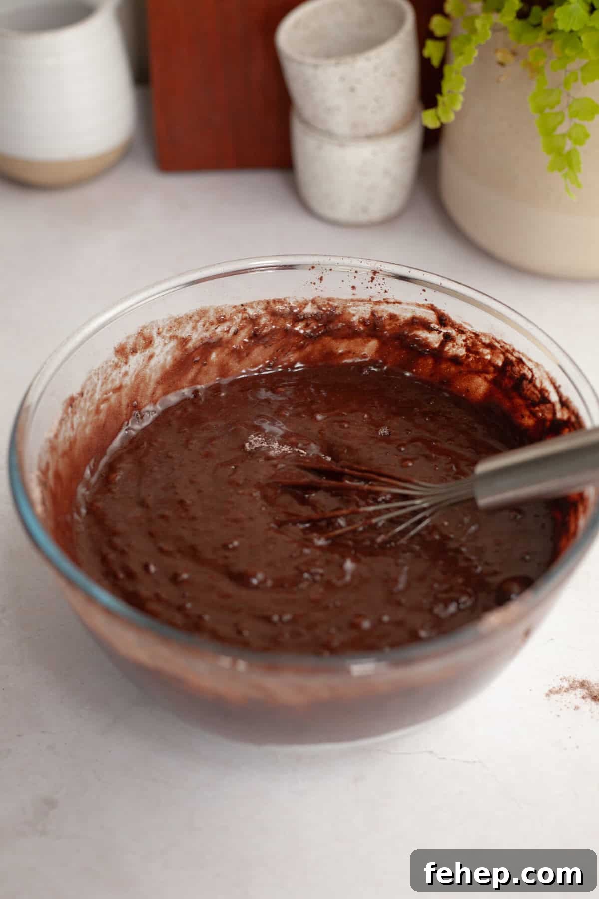 Chocolate cake batter in a glass bowl with a whisk.