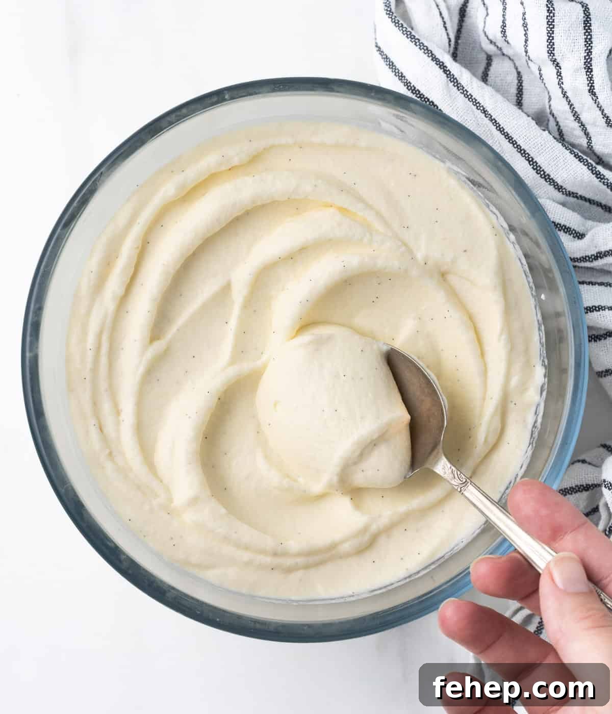 How to Make Classic Chantilly Cream (Crème Chantilly) 7 Cream in a large mixing bowl with a silver spoon, seen from above.