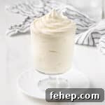 How to Make Classic Chantilly Cream (Crème Chantilly) 10 Cream piped inside a glass cup over a small white plate with a striped tea towel in the background.