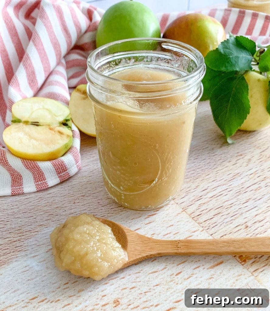 Homemade Unsweetened Applesauce Recipe — Simple & Natural 9 A jar of applesauce. A wooden spoon and apples in the background.