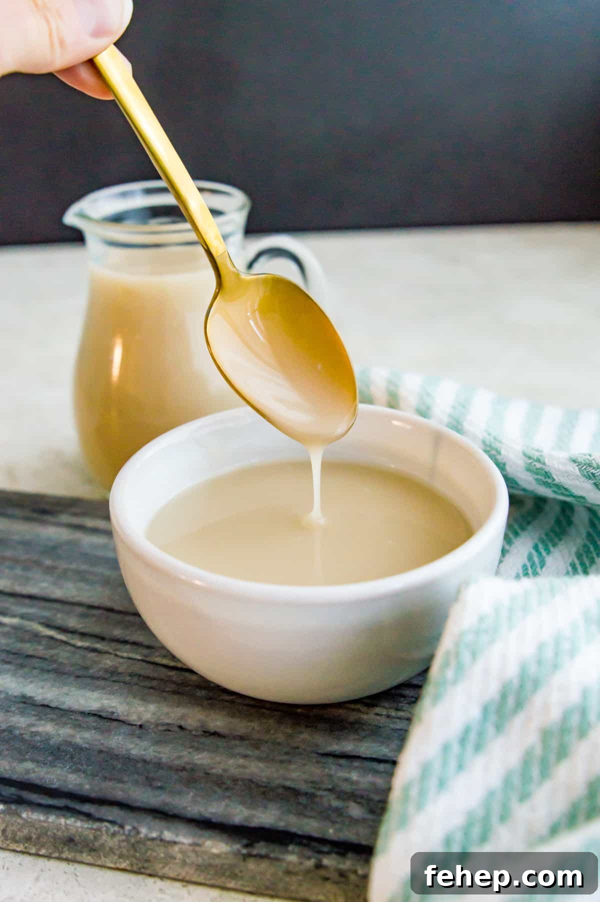 A bowl of coconut condensed milk with a spoon in it and a bottle of more condensed milk beside it.
