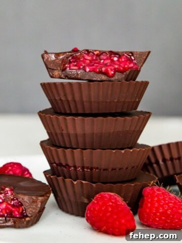 A stack of five chocolate raspberry cups and the top one has a bite out of it so you can see the raspberry filling.