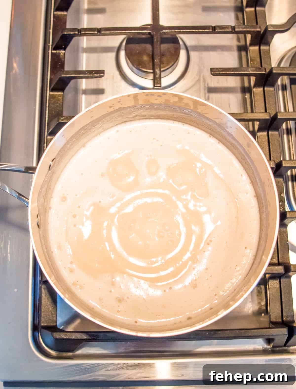 A pot on the stovetop with boiling coconut milk in it.