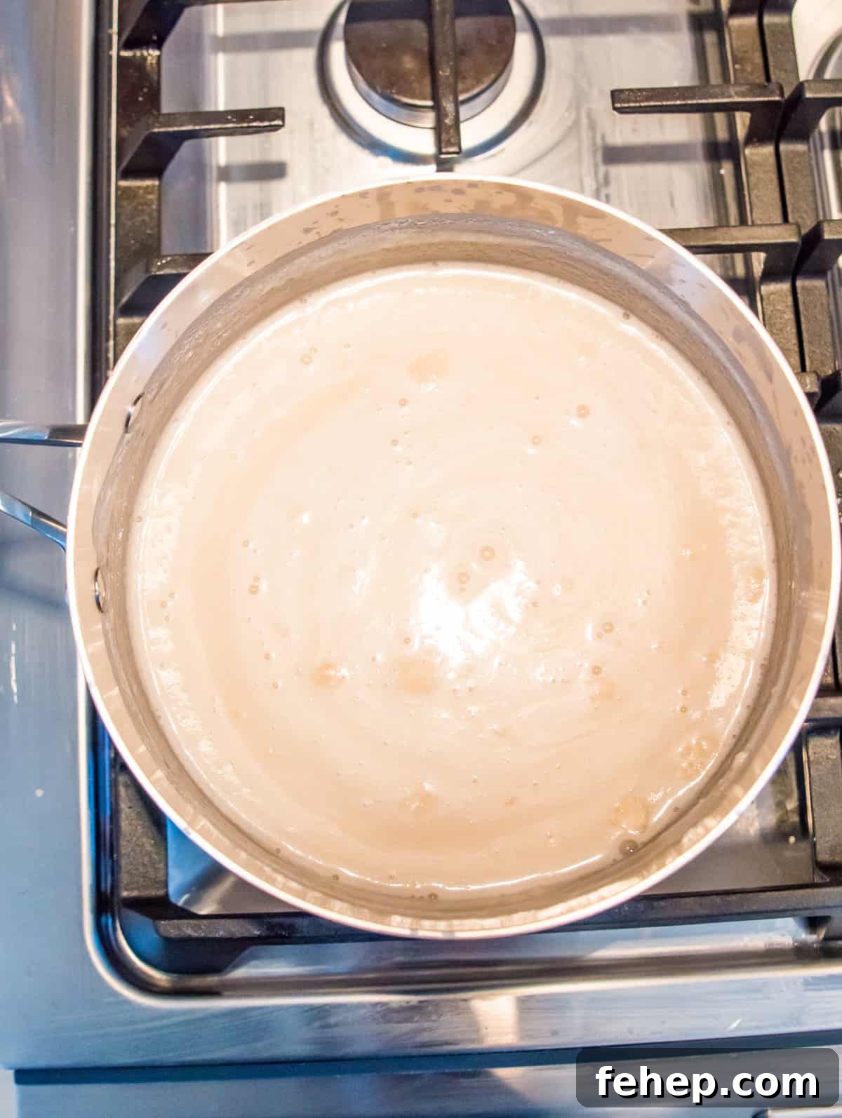 A pot on the stovetop with coconut milk simmering in it.