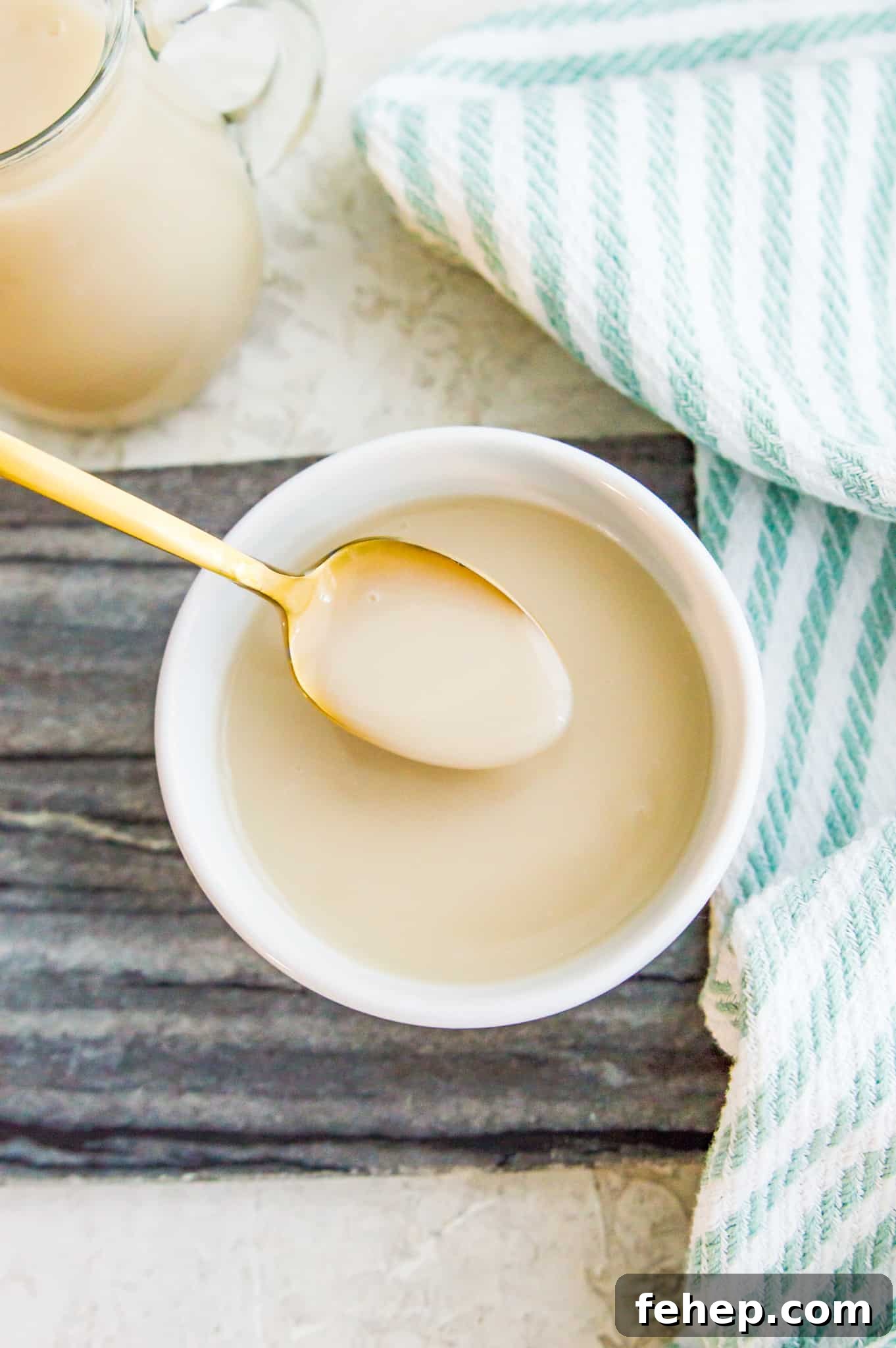 A bowl of condensed milk with a spoon in it and a tea towel next to the bowl.