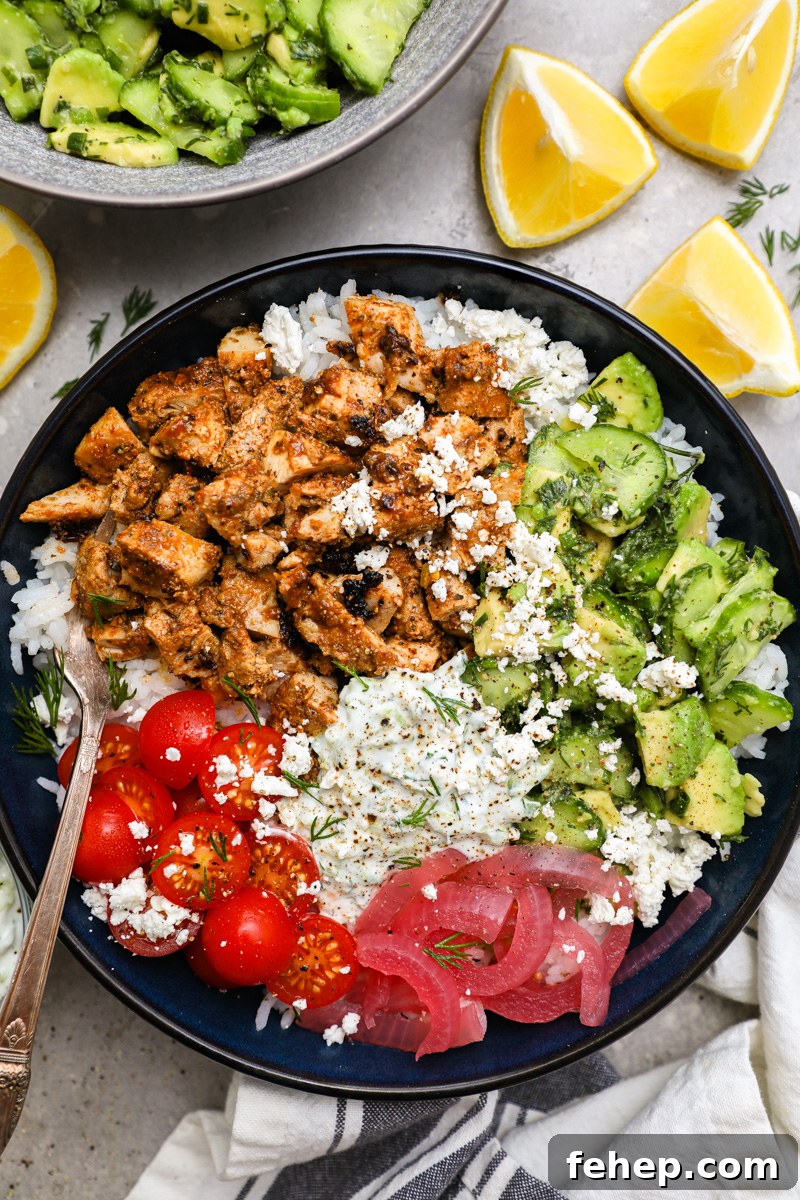 A large blue blue filled with white rice, pickled onion, tomato, marinated chicken, homemade tzatziki and cucumber-avocado salad