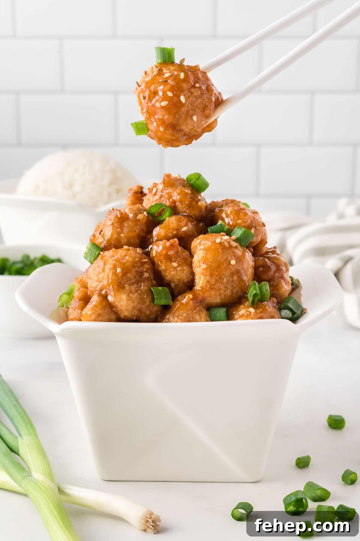 Sticky Teriyaki Cauliflower Bites with Sesame and Scallions 2 chopsticks taking a bite of cauliflower from the container