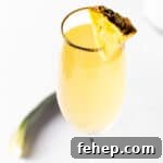 A pineapple mimosa in a champagne flute, garnished with a pineapple slice.