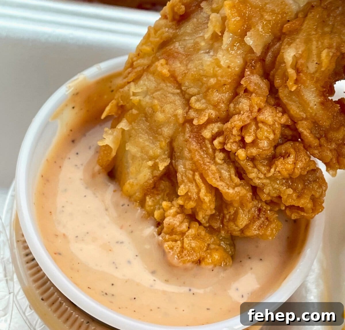 Copycat Raising Cane’s Sauce Recipe: Homemade Cane’s Dipping Sauce 2 Golden fried chicken piece partially submerged in a creamy dipping sauce in a plastic cup.