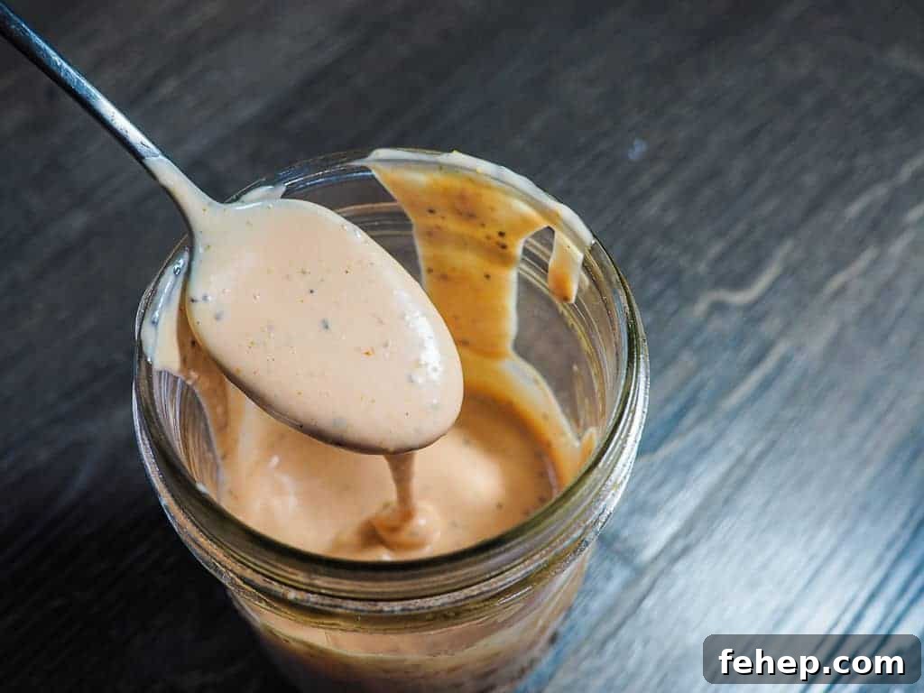Copycat Raising Cane’s Sauce Recipe: Homemade Cane’s Dipping Sauce 8 A jar of light orange Raising Cane's dipping sauce with a metal spoon on a gray wooden background.