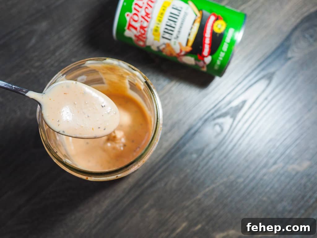 Copycat Raising Cane’s Sauce Recipe: Homemade Cane’s Dipping Sauce 9 A jar of light orange Raising Cane's dipping sauce with a metal spoon and a jar of Tony Chachere's Creole Seasoning on a gray wooden background.