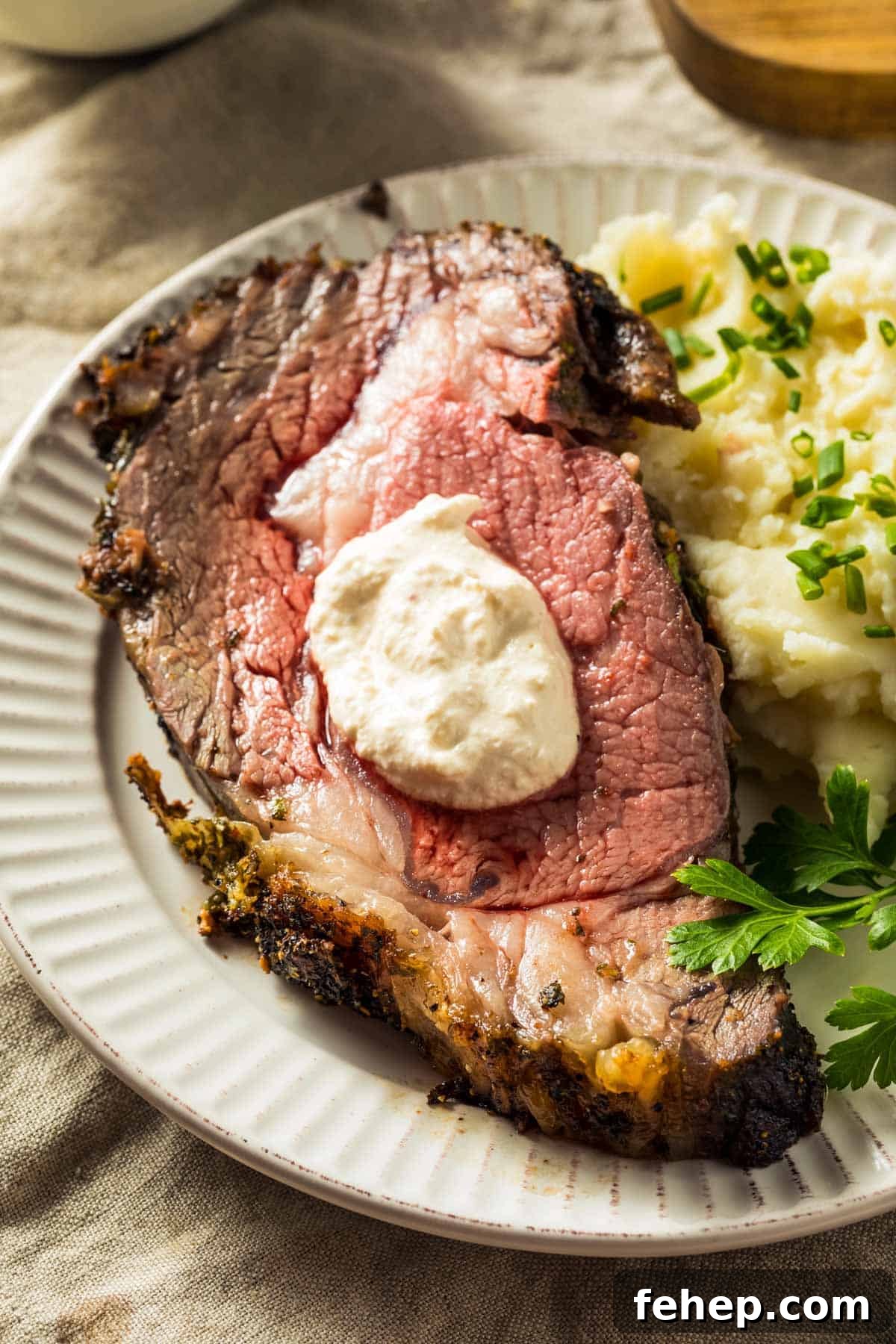 Garlic-Herb Crusted Boneless Prime Rib Recipe 2 a slice of boneless prime rib topped with creamy horseradish sauce, on a white plate with mashed potatoes