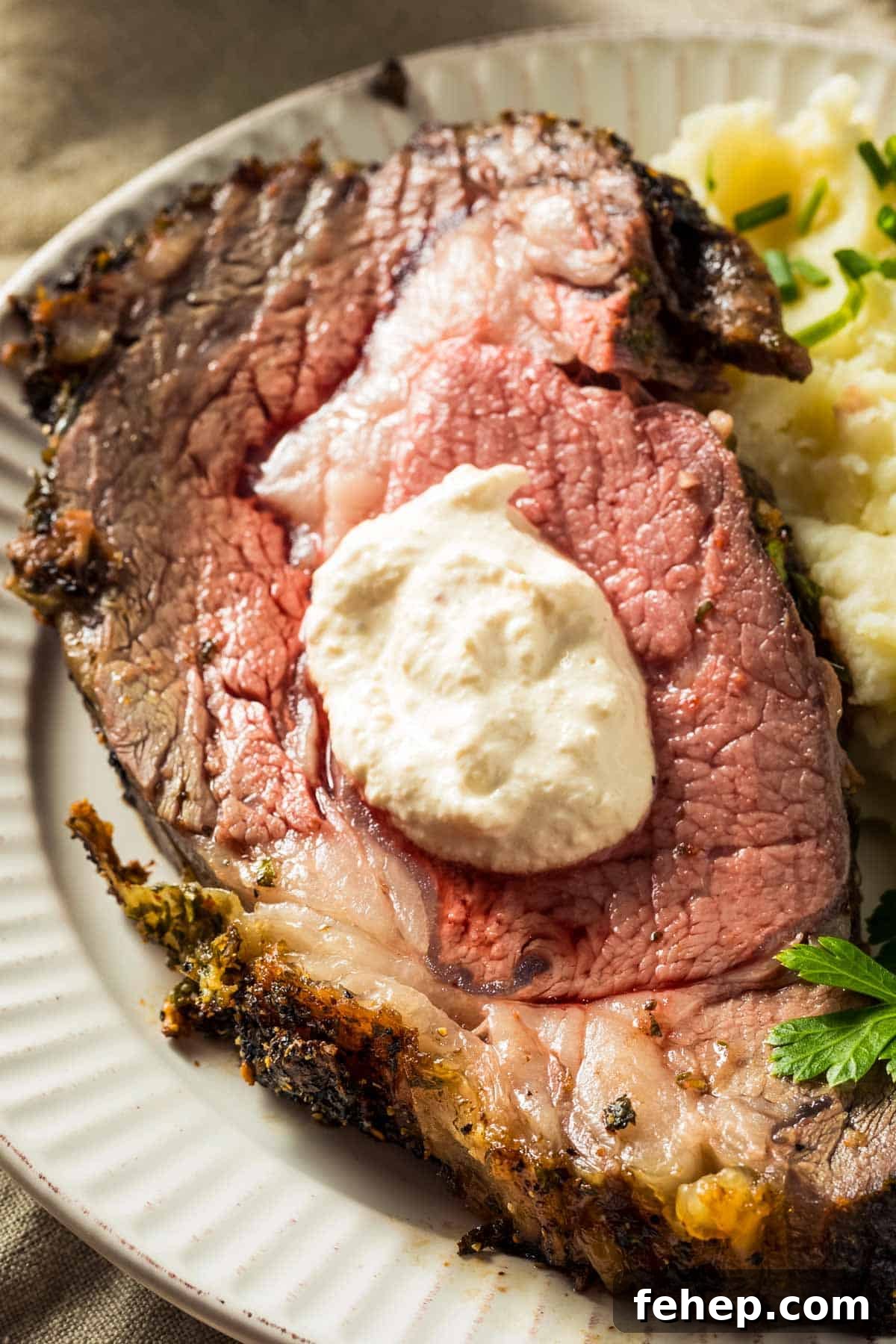 Garlic-Herb Crusted Boneless Prime Rib Recipe 5 a closeup of a slice of boneless prime rib topped with creamy horseradish sauce, on a white plate
