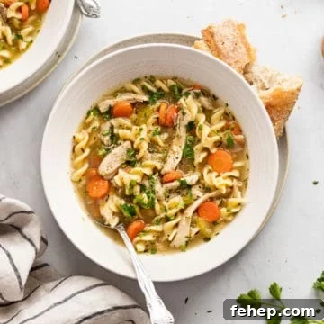 Close-up of a bowl of chicken soup from scratch with a spoon, with a torn baguette alongside.