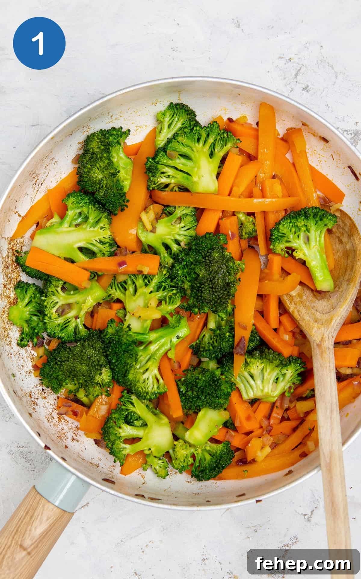 Broccoli and carrots in a frying pan with a wooden mixing spoon.