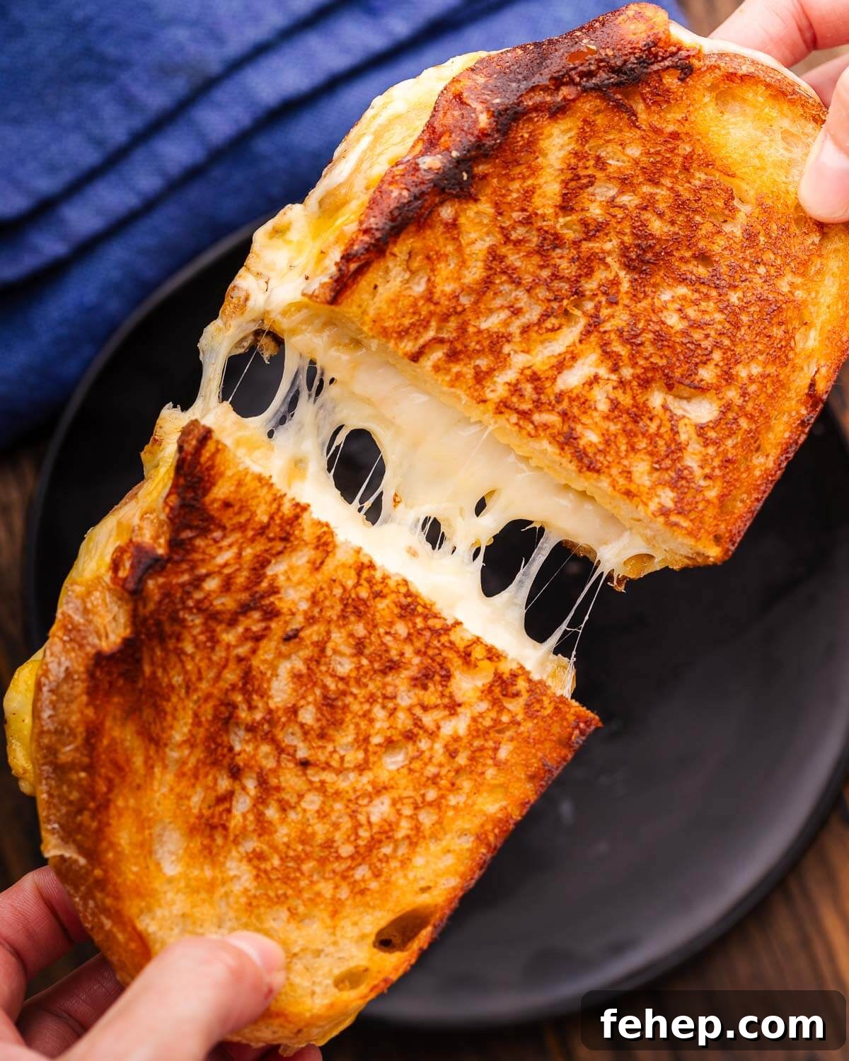 Hands pulling apart grilled cheese over black plate.