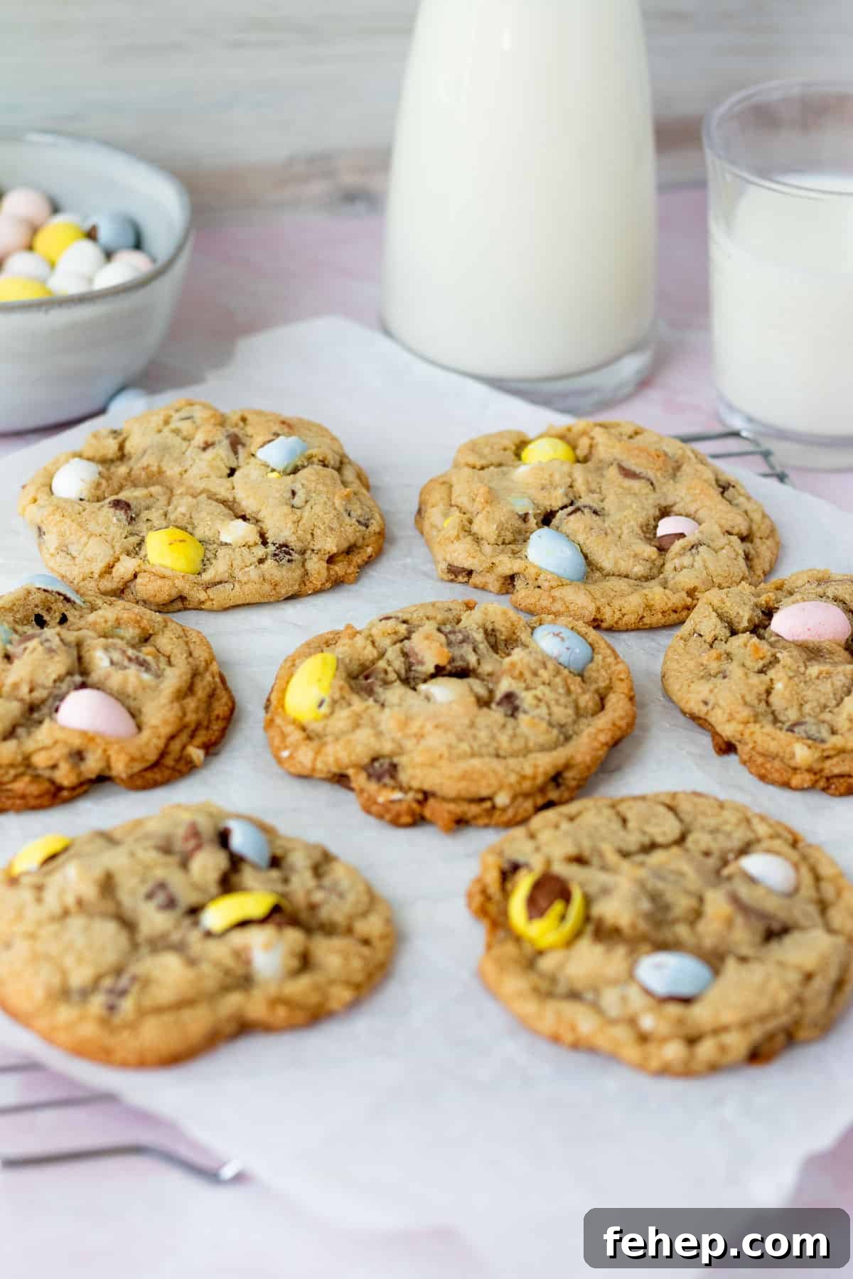 mini egg cookies  on parchment paper with glasses of milk in background with bowl of mini egg candies