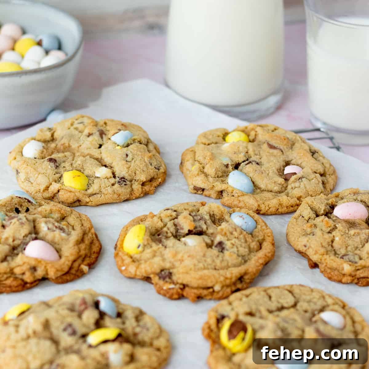 mini egg cookies on parchment paper with glasses of milk in background with bowl of mini egg candies