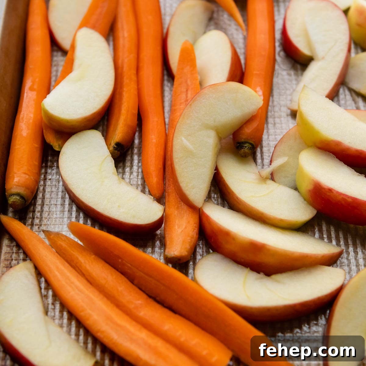 Maple Dijon Roasted Carrots and Apples with Honey Glaze 3 cut, unbaked carrots and apples on a baking pan.