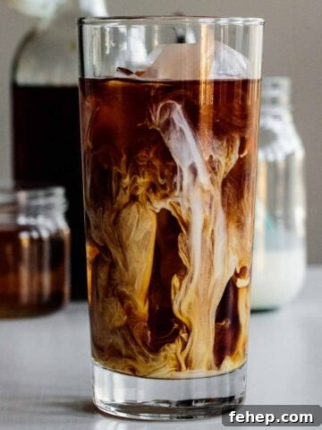 a tall glass of vanilla sweet cream cold brew with cream, syrup and coffee in the back