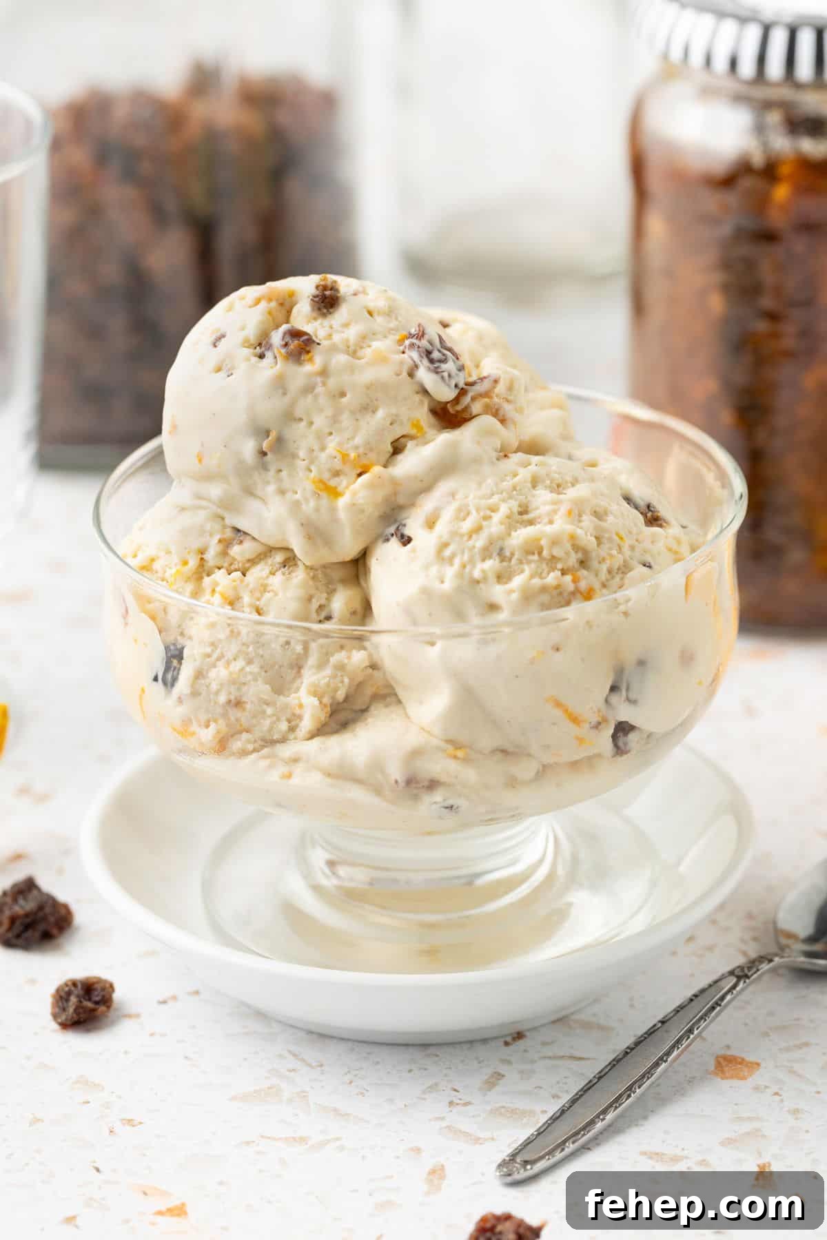 Three scoops of Fruit Mince Ice Cream in a glass bowl, sitting on a small white plate, with a silver spoon on the edge.