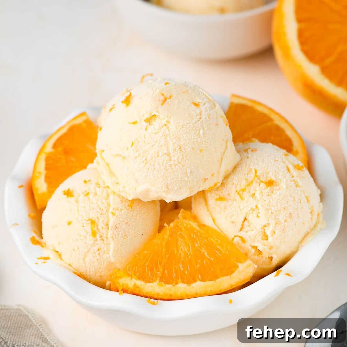 Round white bowl of ice cream with three scoops and some orange pieces.