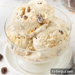 Four scoops of Fruit Mince Ice Cream in a glass bowl, sitting on a small white plate, with a silver spoon on the edge.