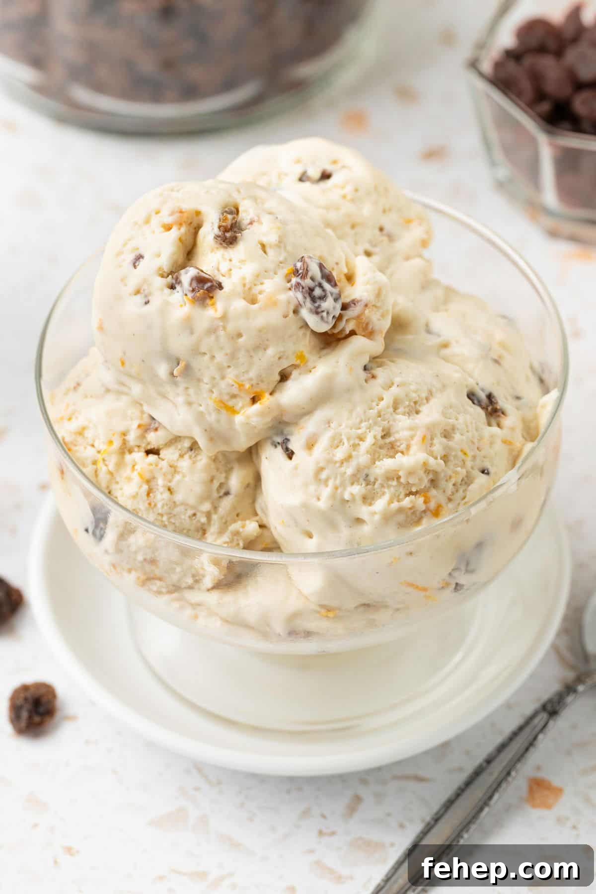 Four scoops of Fruit Mince Ice Cream in a glass bowl, sitting on a small white plate, with a silver spoon on the edge.