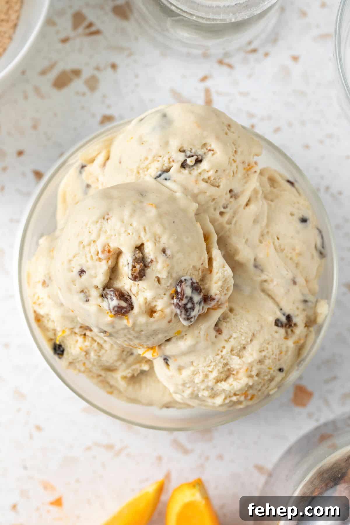 Four scoops of Fruit Mince Ice Cream in a glass bowl, sitting on a small white plate, with a silver spoon on the edge.