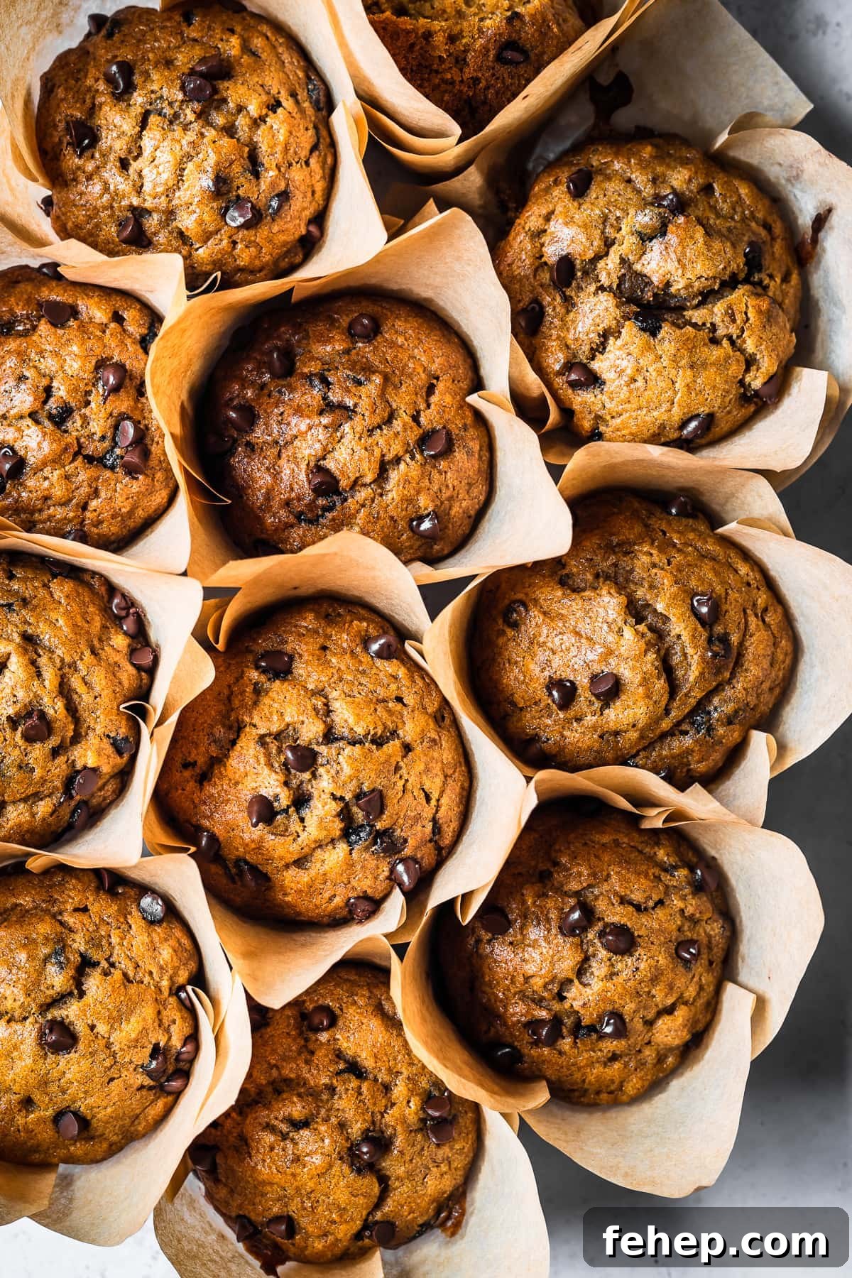 A closeup view of eleven pumpkin banana muffins nestled next to each other in brown parchment paper liners.