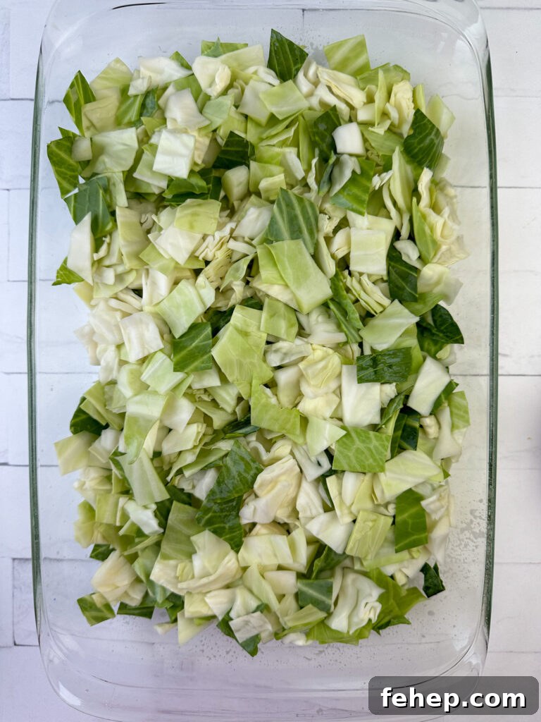 Half a head of raw, coarsely chopped cabbage in a 9 x 13 casserole dish on a white counter top.