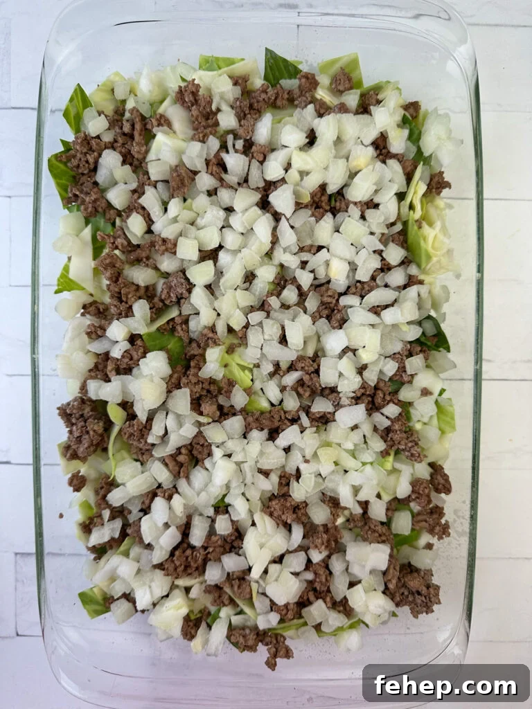Chopped onion spread over hamburger in a layer on top of chopped cabbage in a casserole dish.