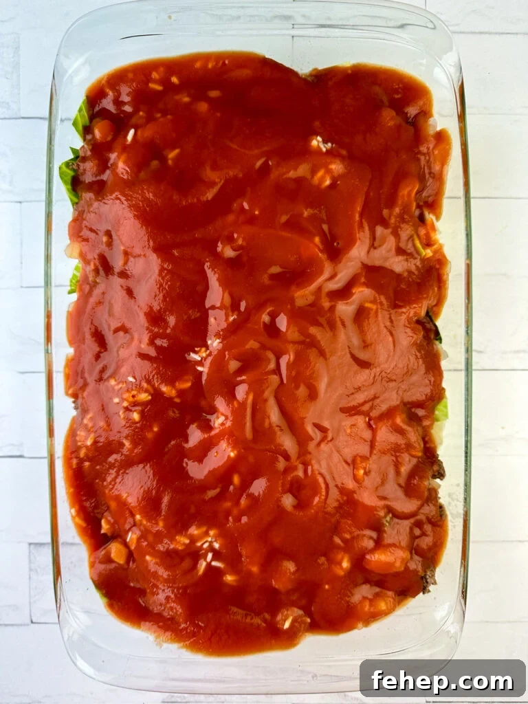 Two cans of tomato sauce poured over top of layers of rice, ground beef, onions and cabbage in a 9 x 13 casserole dish on a white counter top.