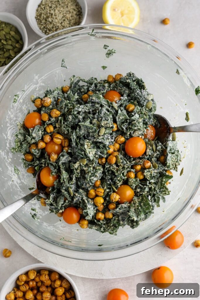Kale Caesar Salad served in a large bowl with two spoons surrounded by crispy chickpeas, cherry tomatoes, hemp hearts, and pumpkin seeds